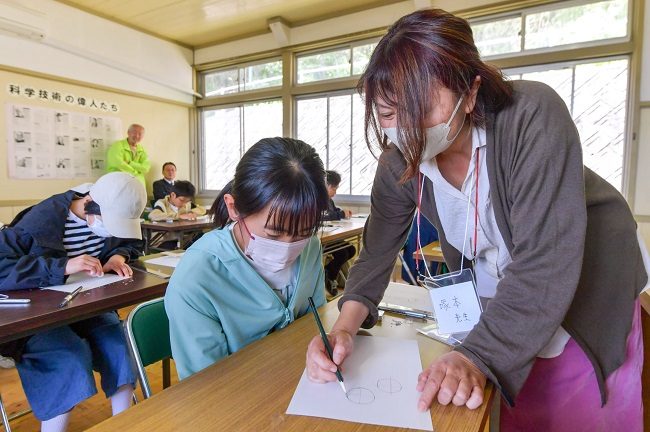 Giáo viên tận tình hướng dẫn các em nhỏ đảo Takaikamishima cách vẽ manga. Ảnh: Kyodo News
